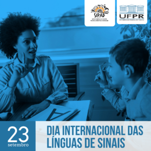 Card para Divulgação do Dia Internacional das Línguas de Sinais: Fotografia com filtro azul.  
A foto apresenta uma professora ensinando LIBRAS a um aluno. A professora é uma mulher negra, de cabelos cacheados, que faz um sinal da LIBRAS com a mão. O aluno é uma criança branca, de cabelo curto. Ele faz o mesmo sinal de LIBRAS que a professora está fazendo. Os dois encontram-se numa sala de aula e sentam-se um de frente para o outro. Existe também uma mesa entre eles, na qual encontra-se uma folha, onde está escrito uma letra “A” maiúscula. No Rodapé do Card, encontra-se, em destaque, a data celebrada: 23 de setembro – Dia Internacional das Línguas de Sinais. Os logos da SIPAD e da UFPR, encontram-se sobre dois retângulos de pontas arredondadas brancos, no topo da imagem.
